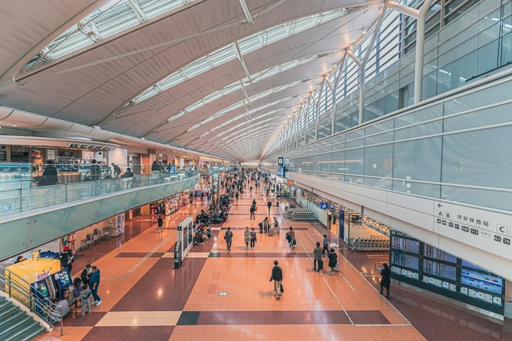 Interior of a spacious airport terminal with passengers walking and shops on multiple levels, representing Tokyo's airports